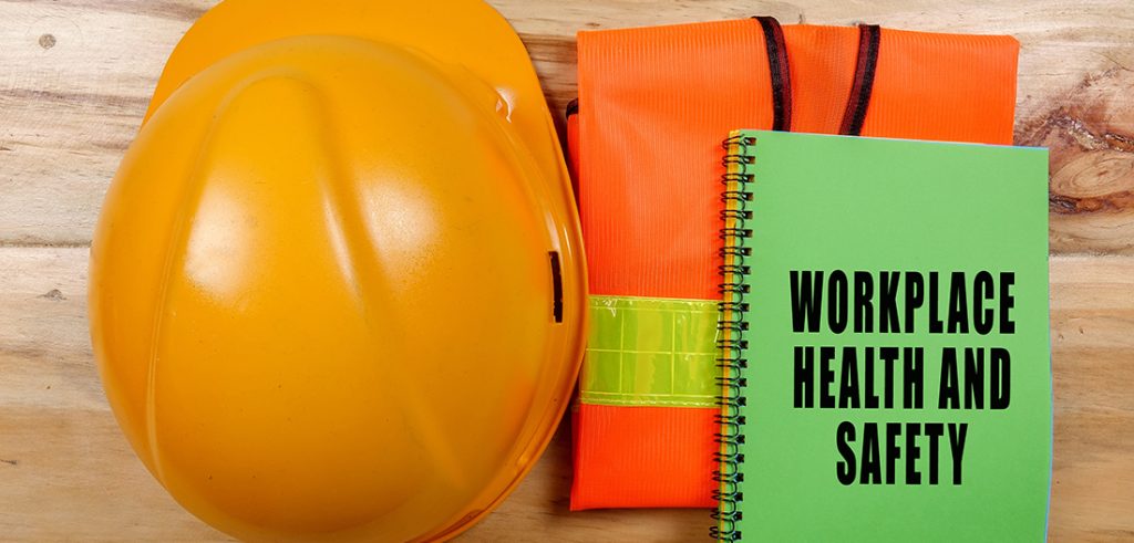 A collection of safety gear including an orange construction hard hat, a bright orange vest with a vibrant yellow stripe, and a green safety handook.