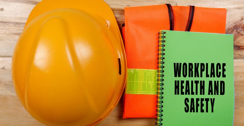 A collection of safety gear including an orange construction hard hat, a bright orange vest with a vibrant yellow stripe, and a green safety handook.